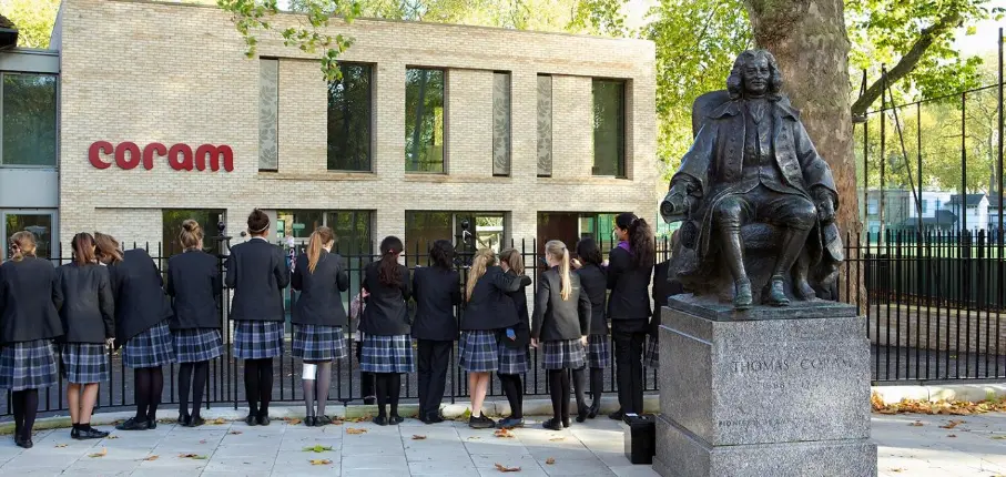 A photo of a status of Thomas Coram, with a group children looking at a building at the Coram campus